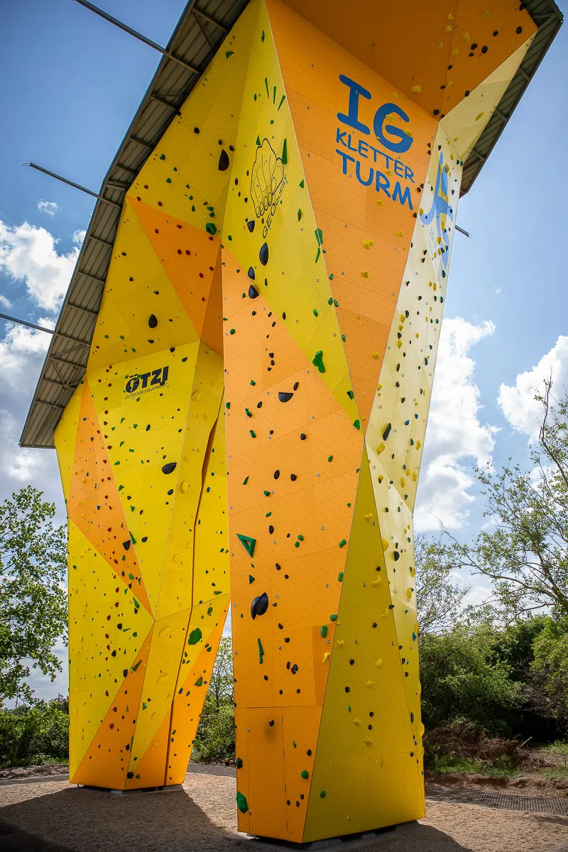 Kletterturm am Thüringer Bahnhof. Ein gelber, überdachter Turm mit bunten Klettergriffen.
