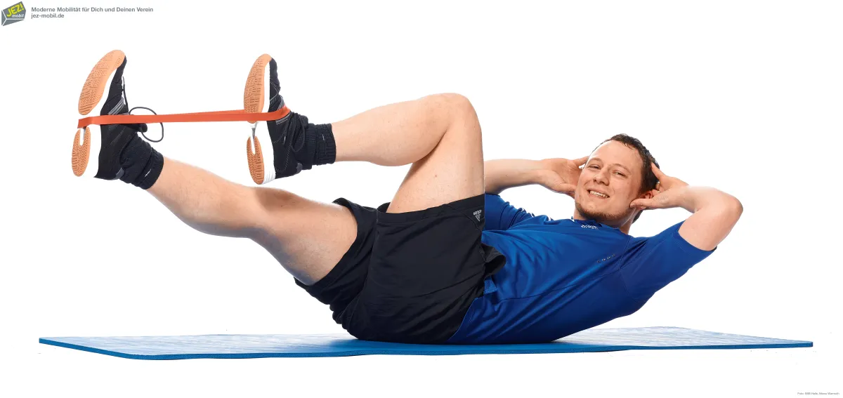 Eine Person auf Gymnastikmatte macht eine Fitnessübung auf dem Rücken liegend mit Gymnastikband an den Beinen.