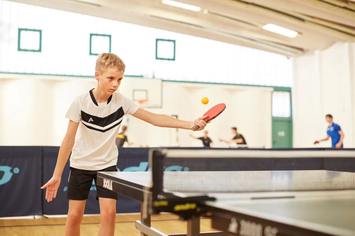 Ein Junge mit Tischtenniskelle an der Platte in Bewegung.