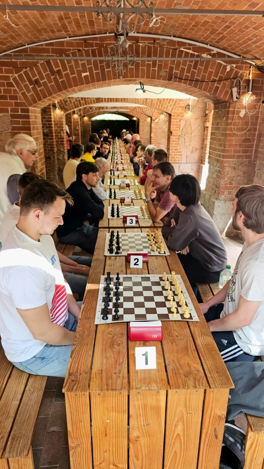 Mehrere Schachspieler liefern sich Duelle an einer langen Tafel.