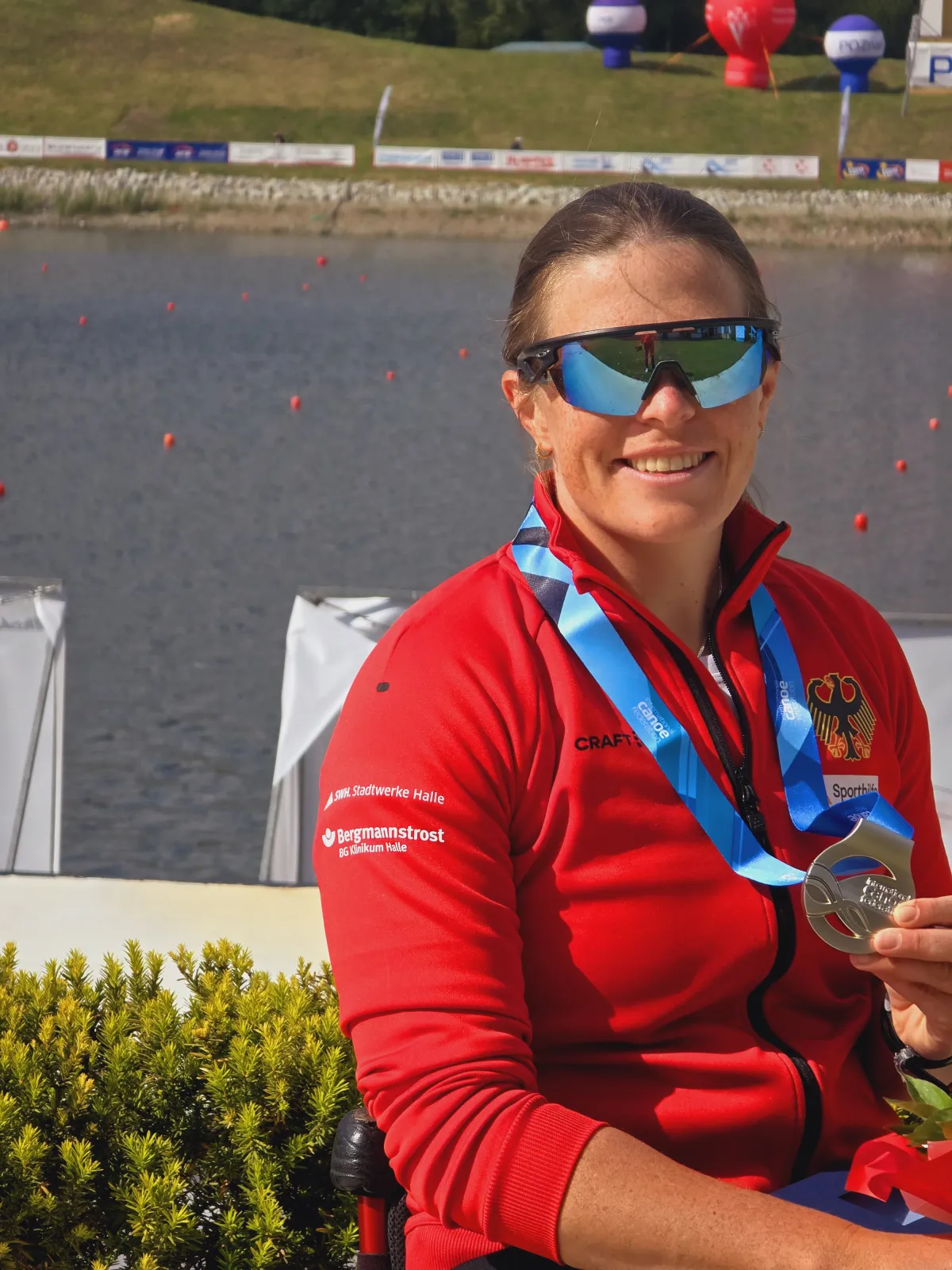 Anja Adler Oberkörperportrait von Anja Adler mit Silbermedaille um den Hals vor einer Regattastrecke.