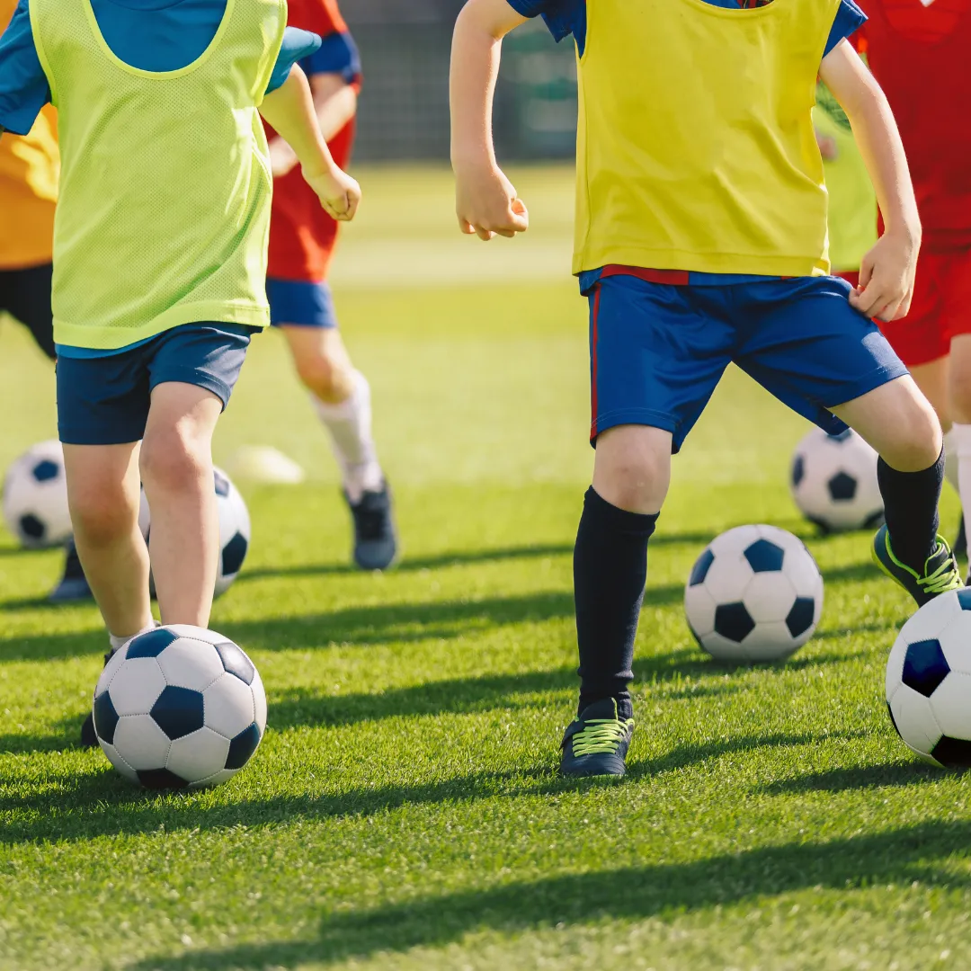 Kindersport Mehrere Kinder in gelben Leibchen dribbeln mit Ball am Fuß. Man sieht die Köpfe nicht.