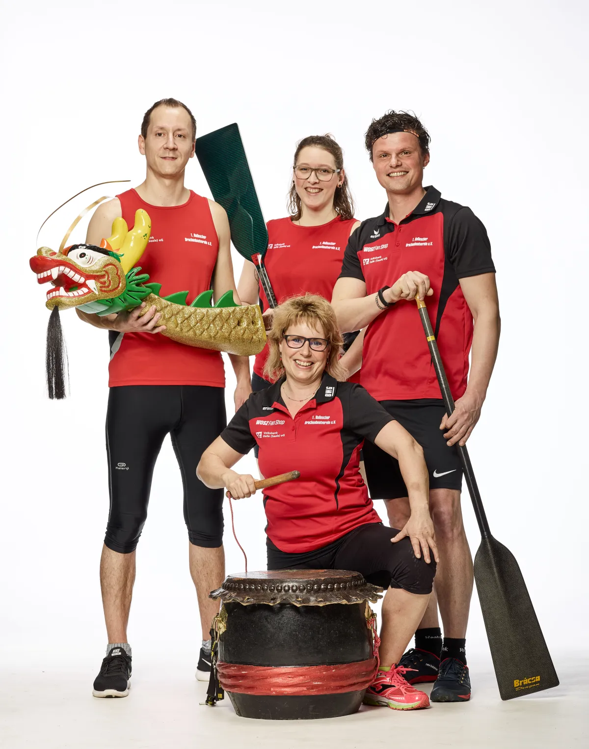 Vier Personen vom Drachenbootverein posieren in roten T-Shirts mit Paddeln, Trommel und Drachenkopf.