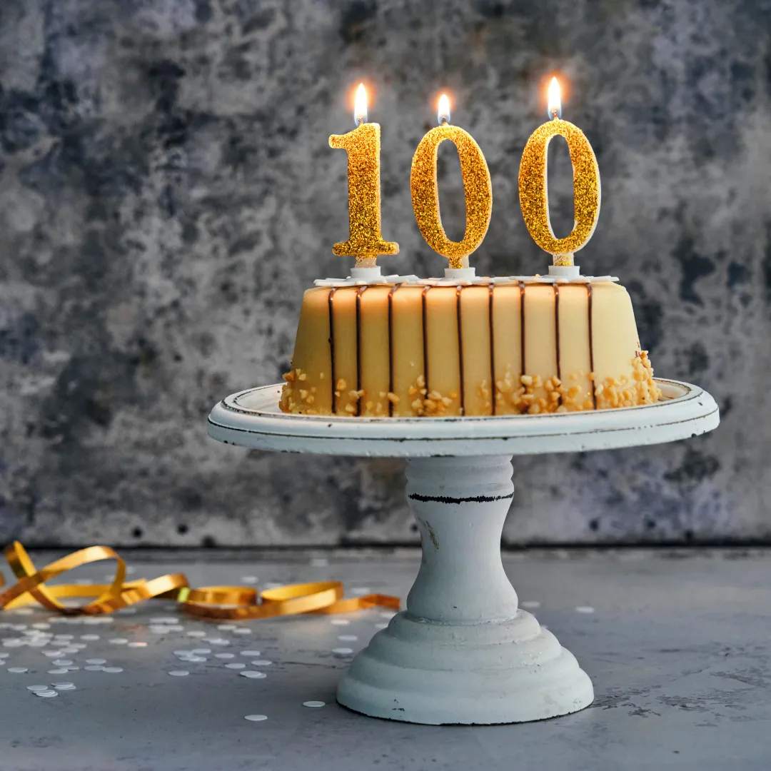 Ein Kuchen auf einer Platte, darauf Kerzen in Form einer Einhundert.