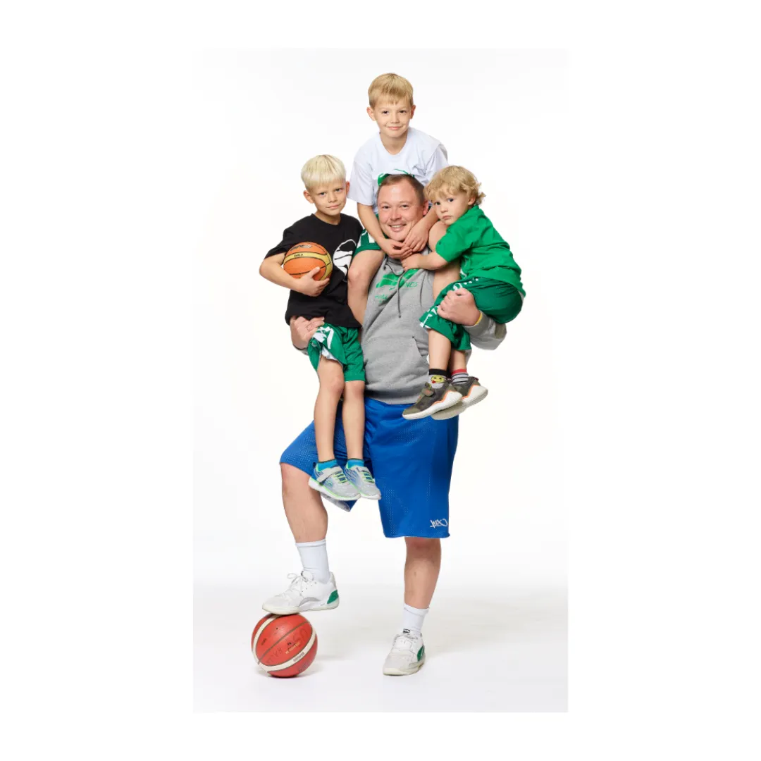 Ein Mann hat drei junge Sportler auf dem Arm und einen Basketball am Fuß.