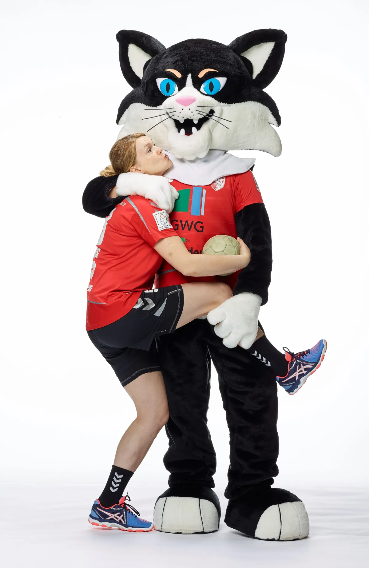 Das Maskottchen der Wildcats - ein Katzenkostüm im Trikot - hält eine Spielerin der Wildcats fest.