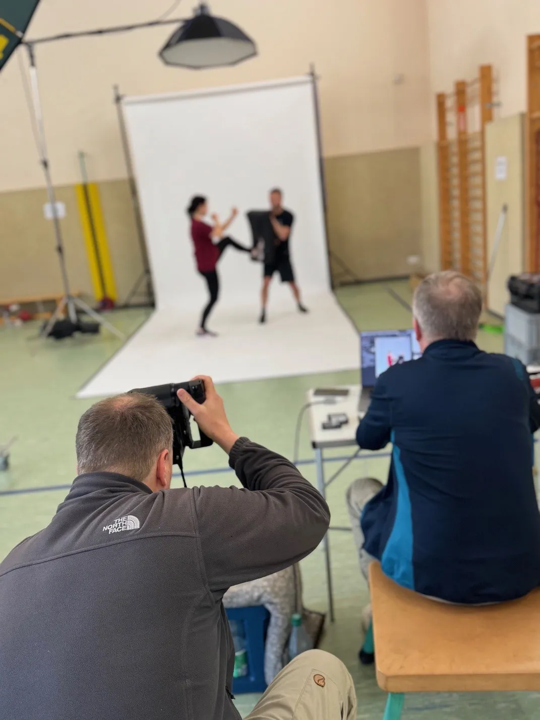 Vor einem Fotohintergrund posen zwei Kampfsportler in Action, man sieht den R&uuml;cken des Fotografen und seines Assistenten