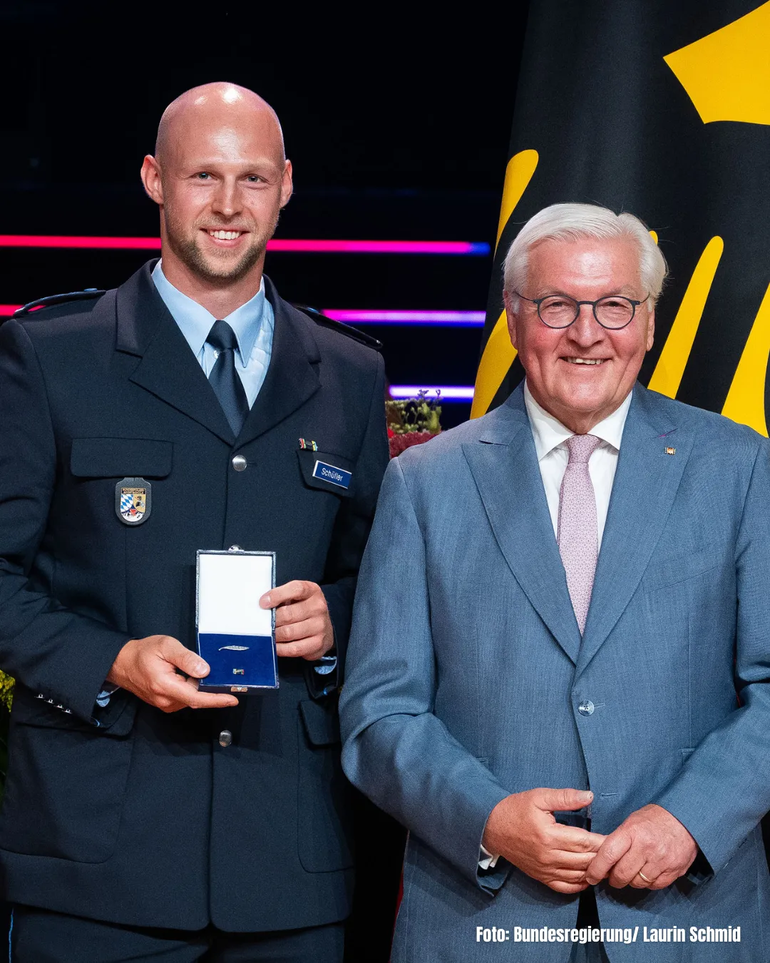 Zwei M&auml;nner in Anzug, einer h&auml;lt eine Auszeichnung, beide gucken in die Kamera
