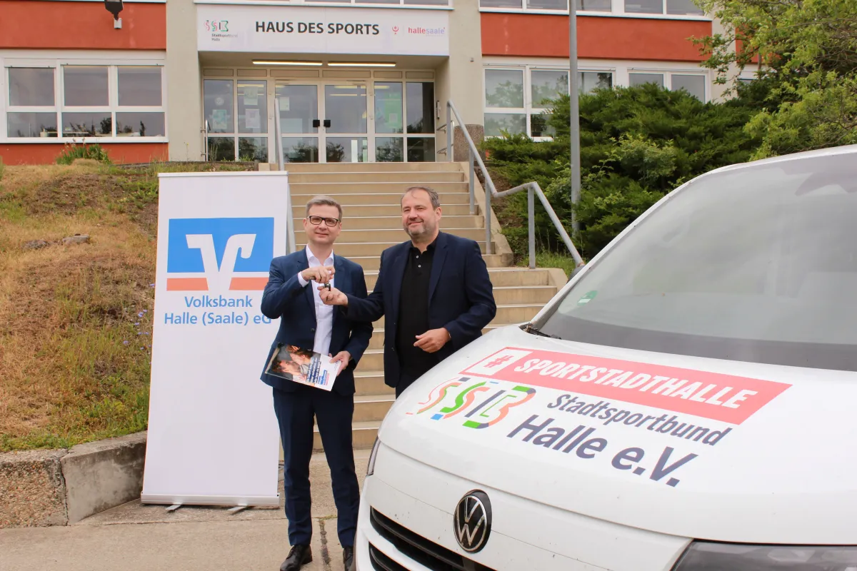 VW-Bus mit SSB-Logo, Volksbank-Rollup und zwei M&auml;nner bei &Uuml;bergabe eines Autoschl&uuml;ssels