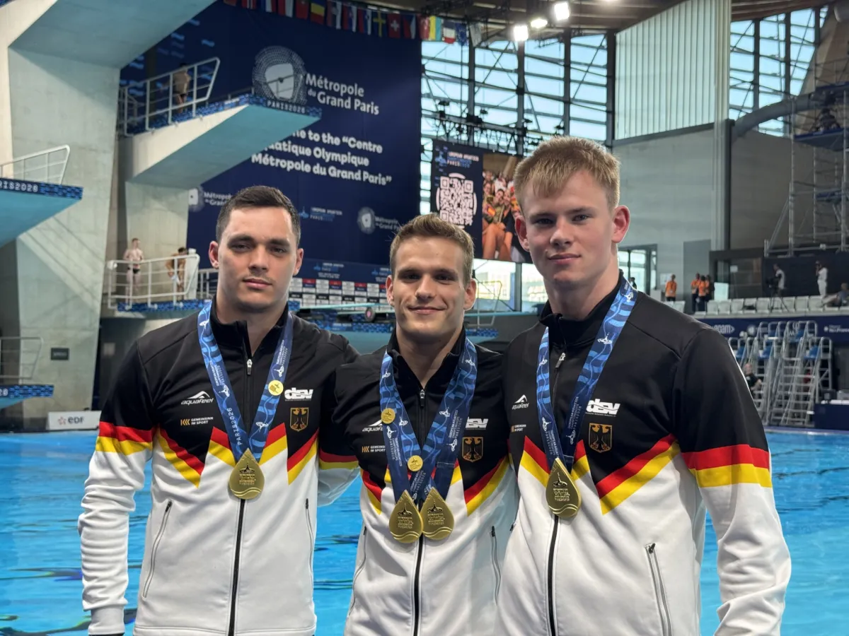 Drei M&auml;nner in Deutschlandtrikots posieren mit Medaille um den Hals vor Sprungturm