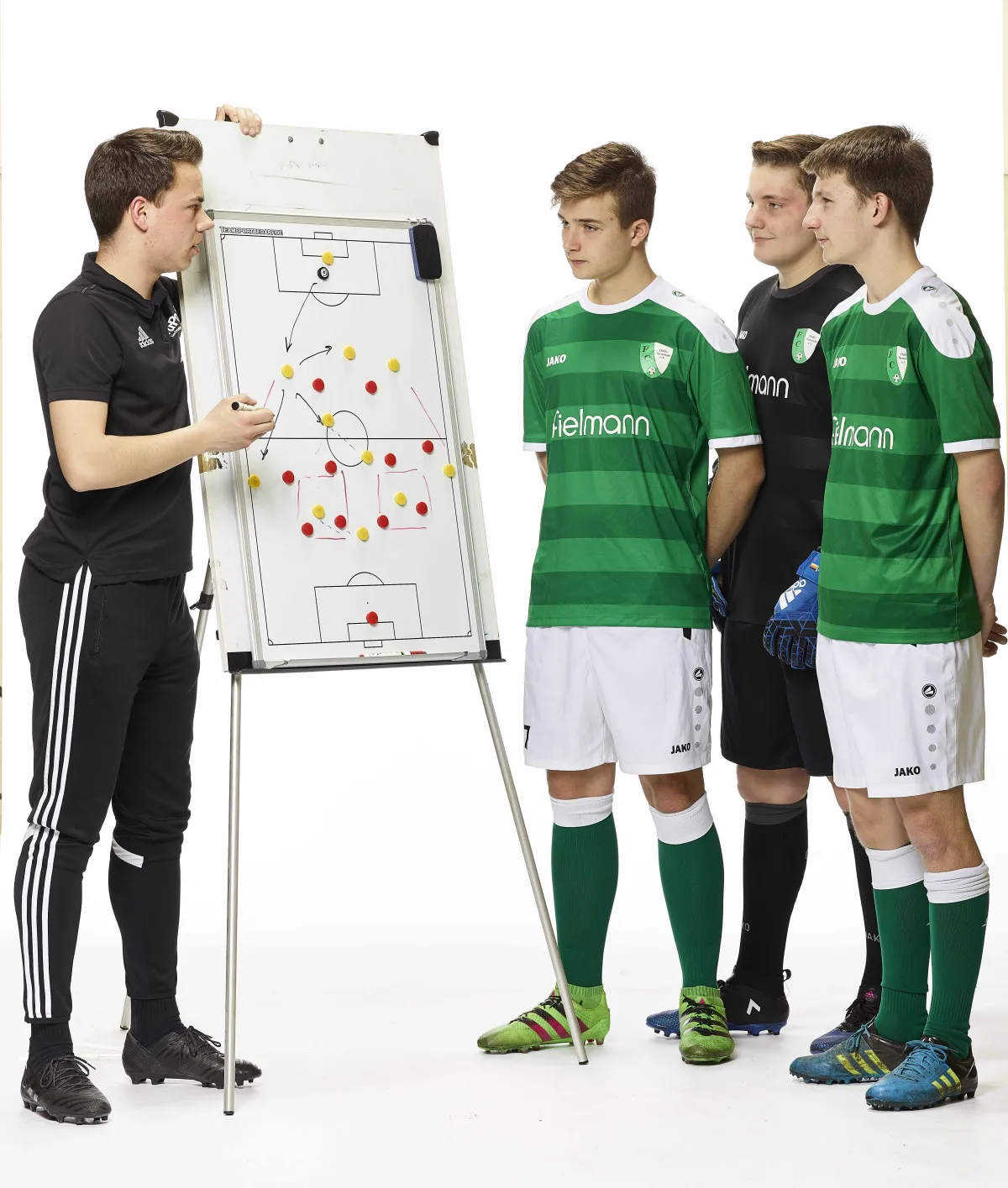Trainer am Taktikboard erkl&auml;rt 3 Jungen im Trikot etwas