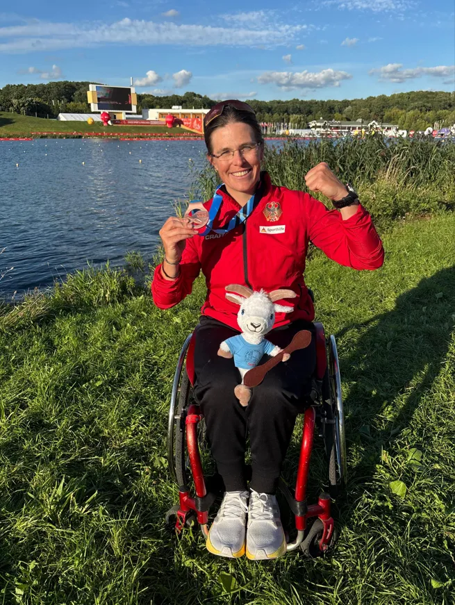 Frau in Rollstuhl zeigt Bronzemedaille