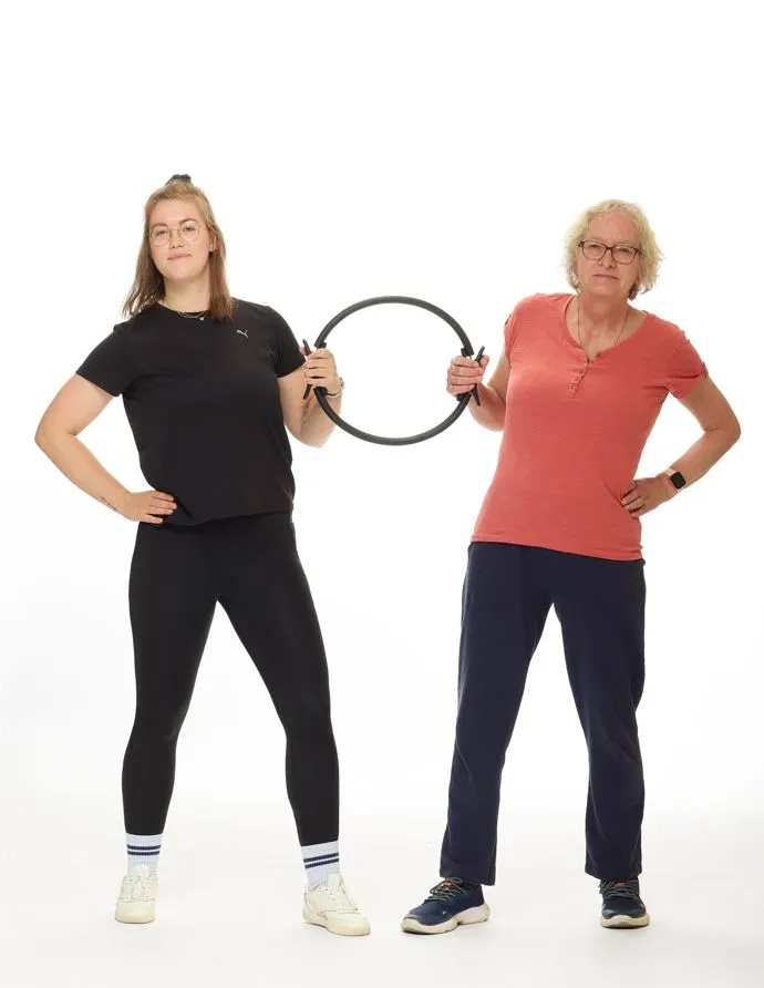 Junge Frau in schwarzer Sportkleidung und &auml;ltere Dame in rosa Sportkleidung ziehen an einem Fitness-Ring.