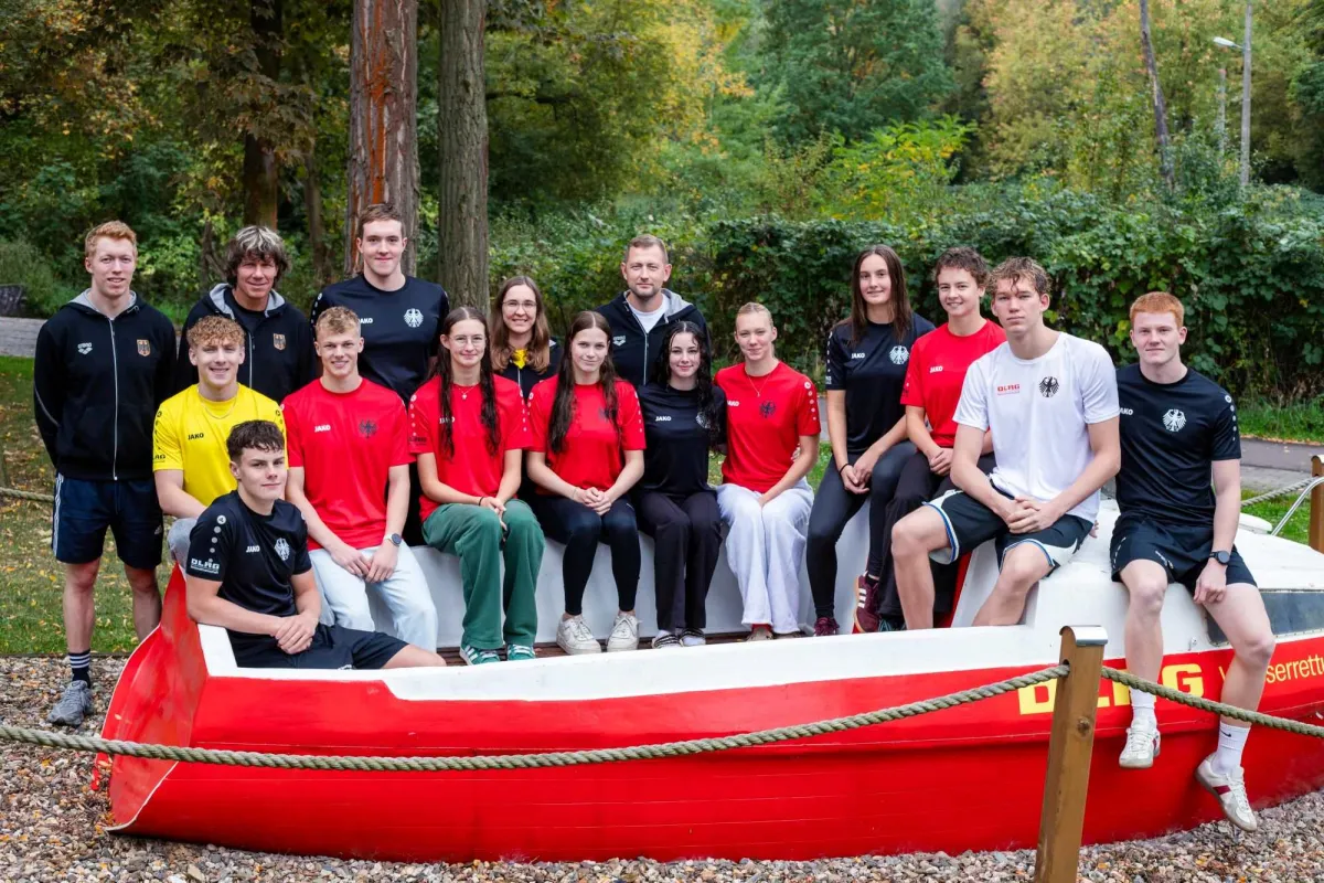 Gruppe junger Menschen in gleichen Shirts hinter einem Rettungs-Boot.