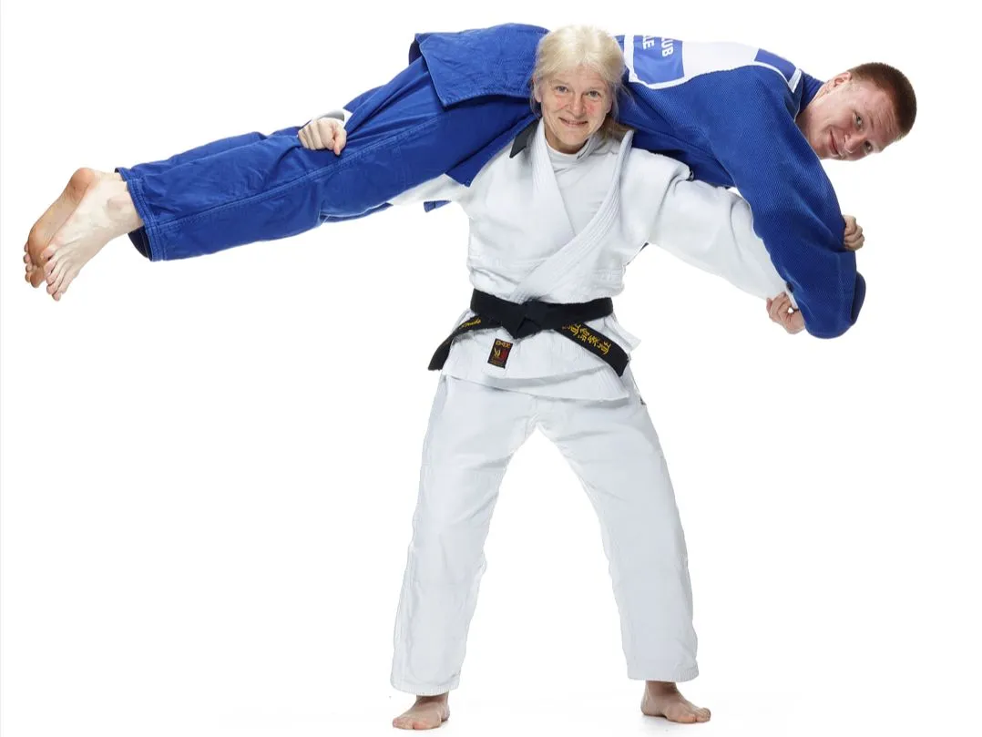 Frau im wei&szlig;en Judoki hebt Mann in blauem Judoki &uuml;ber Schultern