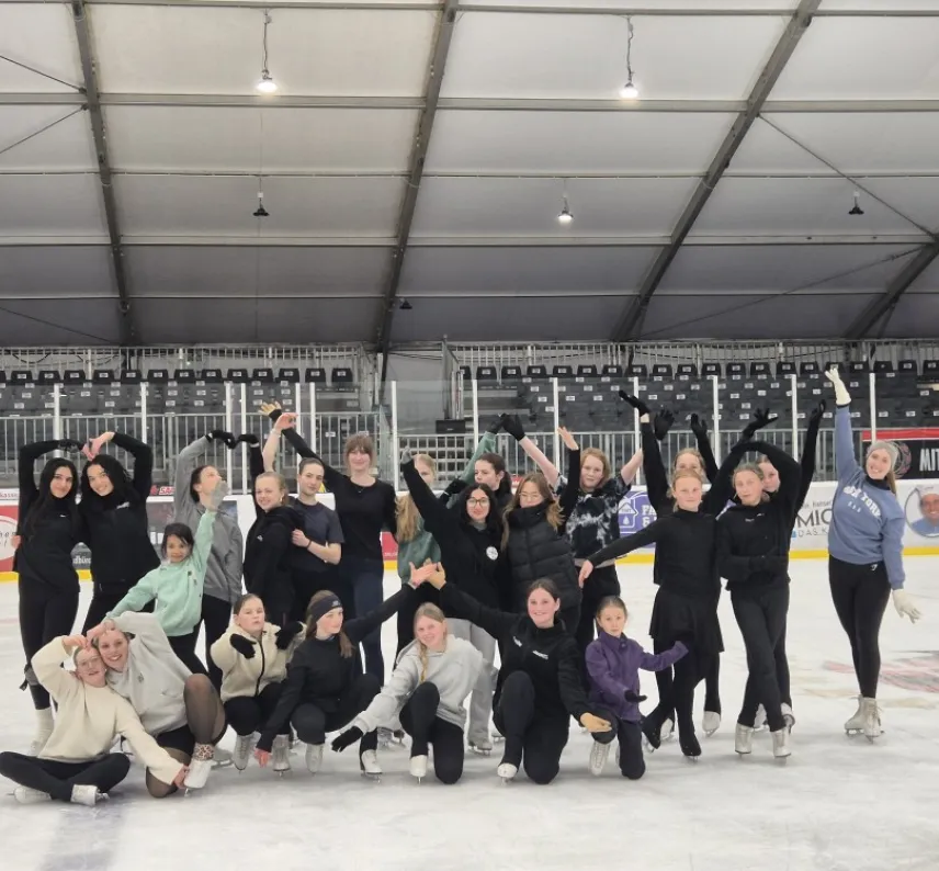 Eine Gruppe von Eiskunstläufer*innen auf dem Eis mit in die Luft gereckten Armen