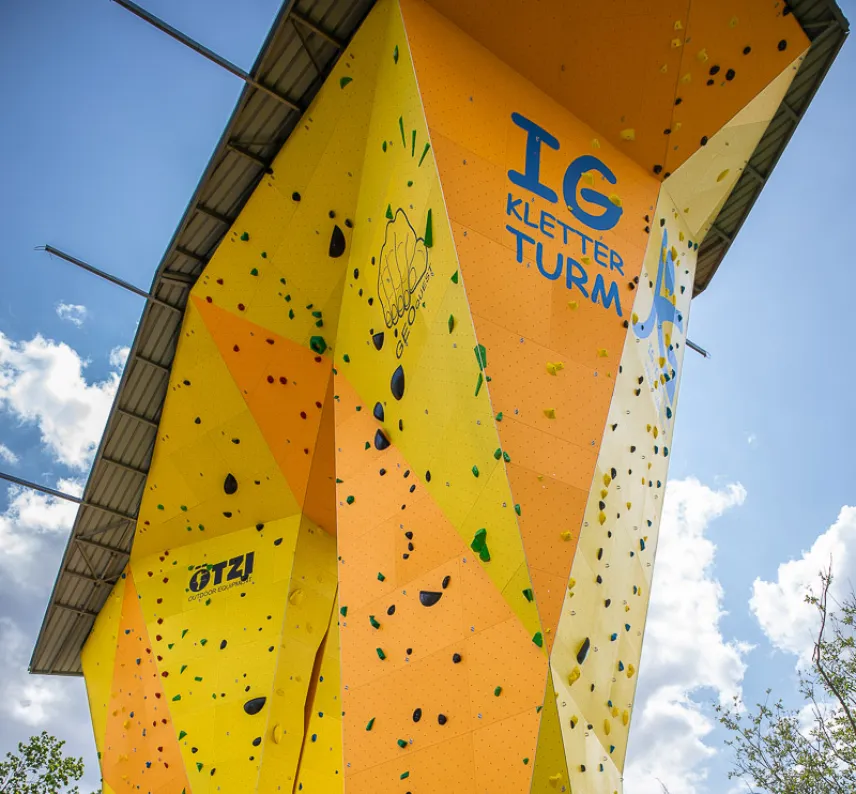 Kletterturm am Thüringer Bahnhof. Ein gelber, überdachter Turm mit bunten Klettergriffen.