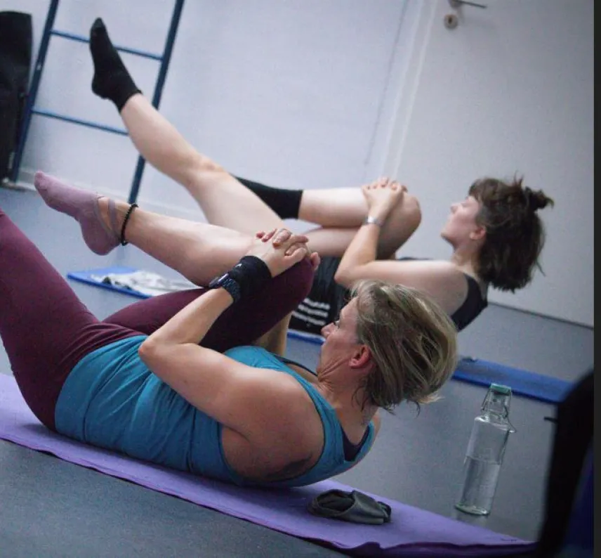 Zwei Frauen auf Gymnastikmatten machen eine Fitnessübung mit angezogenem Bein.