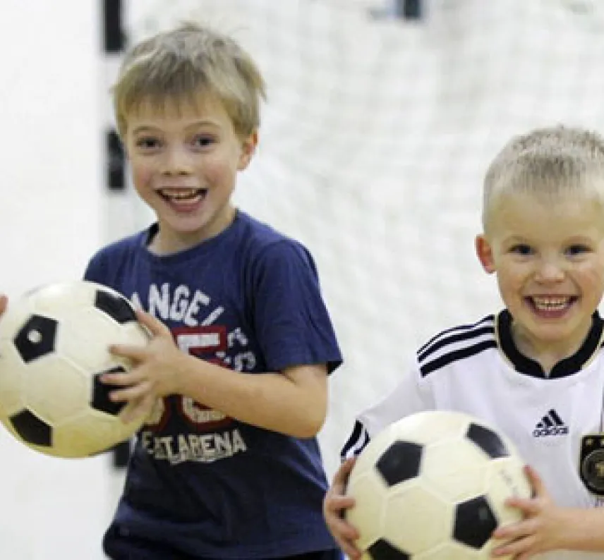 Drei Jungen mit Fußball in der Hand vor einem Handballtor.
