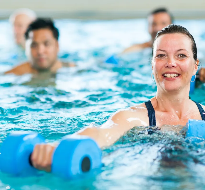 Personen mit Wasserhanteln in einem Schwimmbecken.