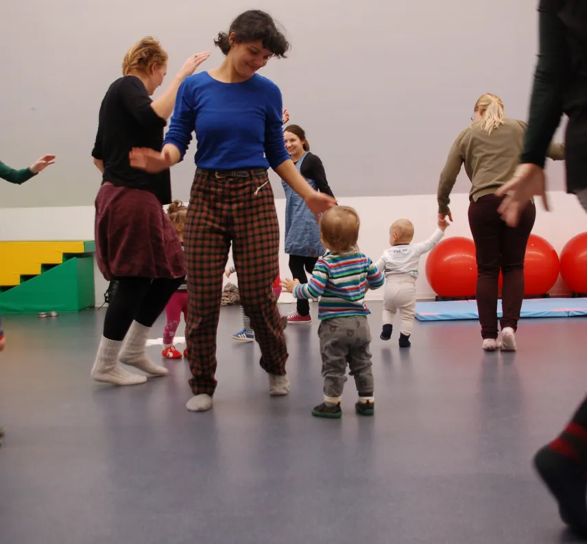 In einem Sportraum laufen mehrere Eltern mit Kleinkindern umher.