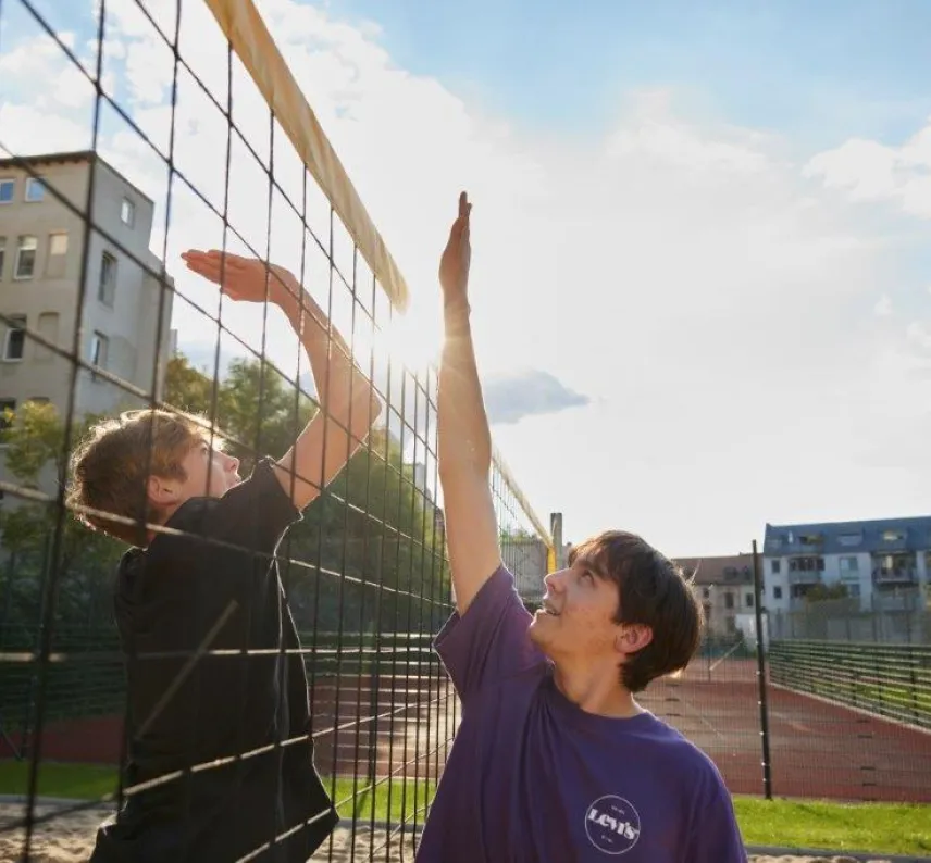 Zwei Personen geben sich über das Volleyballnetz ein High Five. Die Sonne scheint.