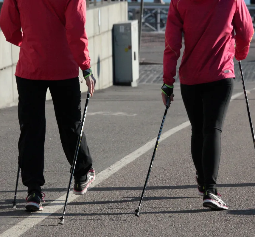 2 Personen in roten Jacken laufen mit Nordic-Walking-Stöcken