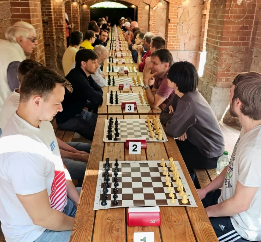 Mehrere Schachspieler liefern sich Duelle an einer langen Tafel.