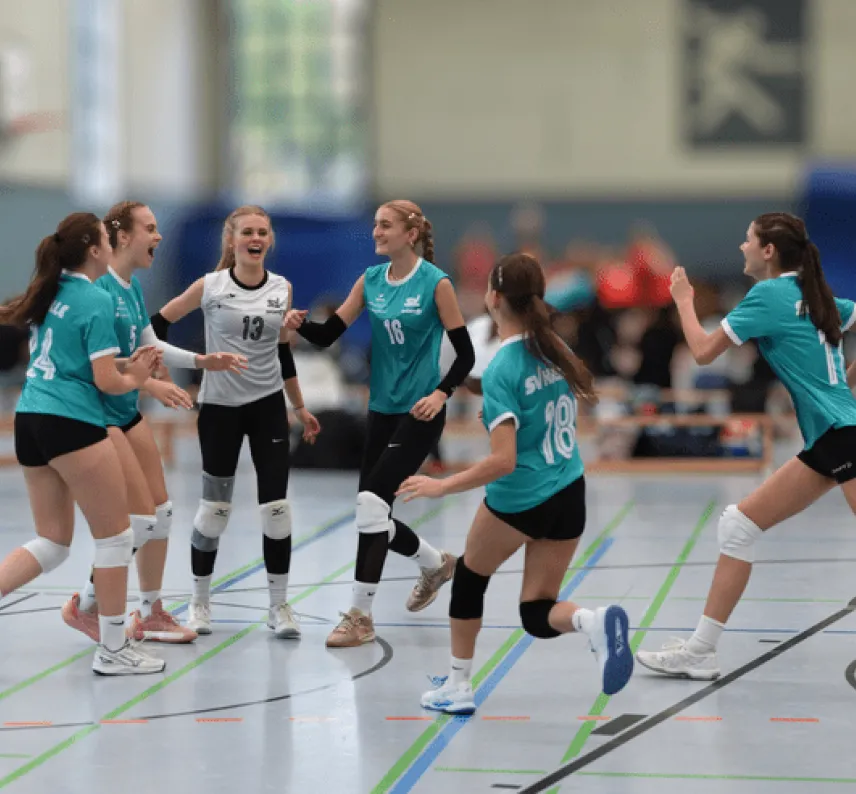 Volleyballerinnen in gr&uuml;nen Trikots und eine in wei&szlig;em Trikot laufen freudig aufeinander zu