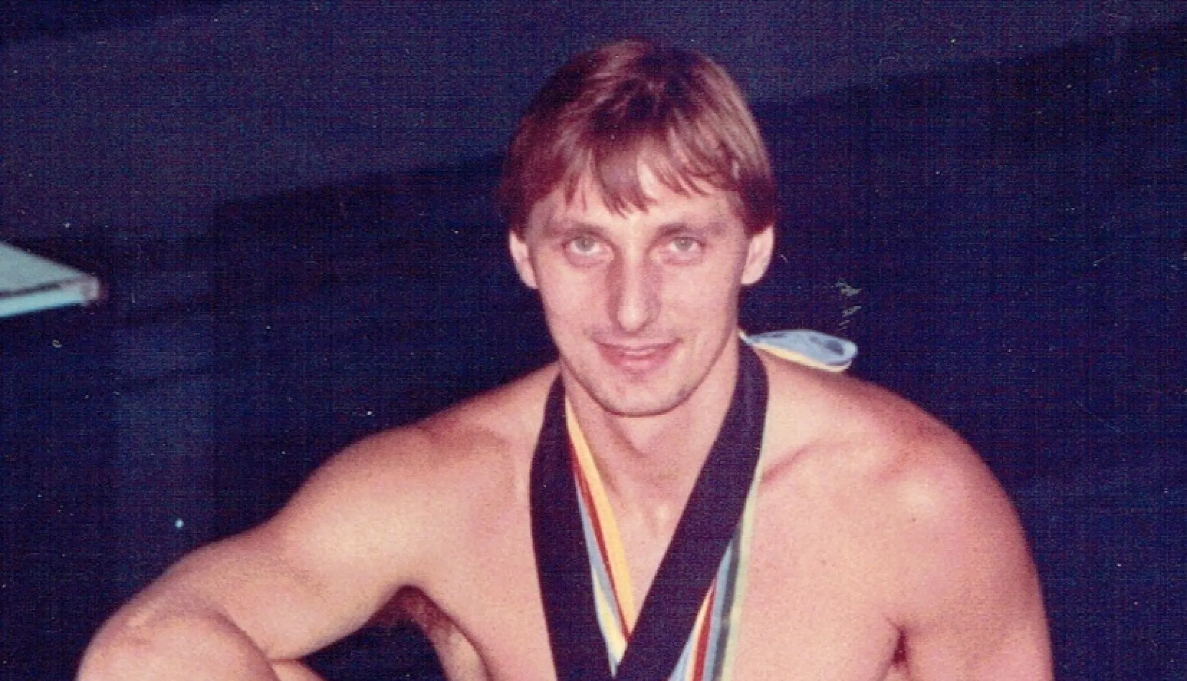 Hoffman in Badehose mit Medaillen um den Hals auf einem Sprungbrett sitzend.