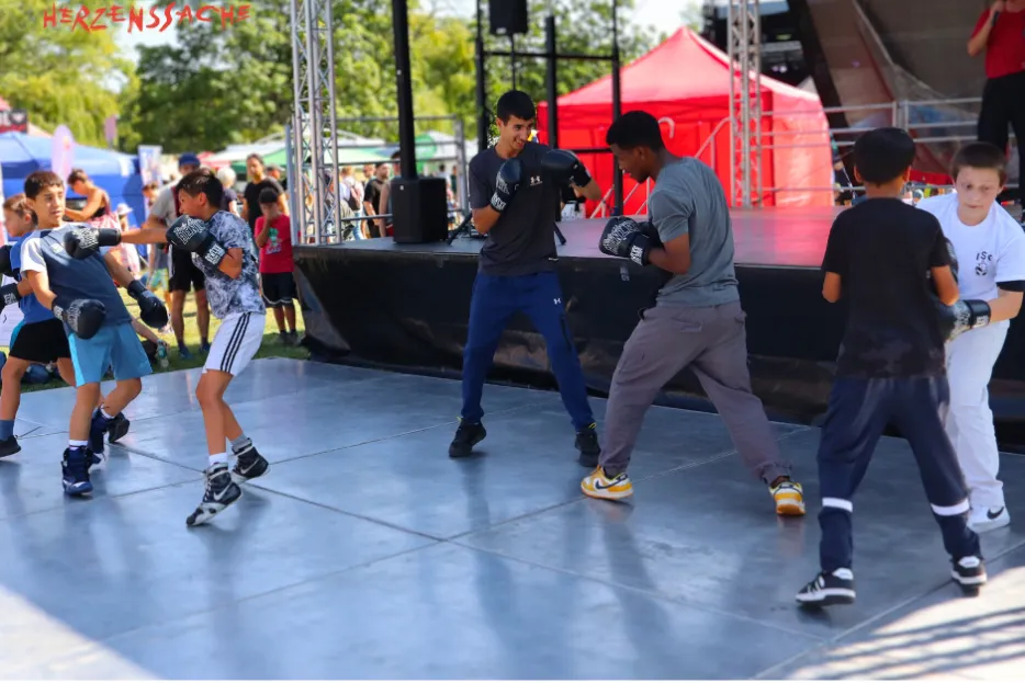 Mehrere Jungen stehen mit Boxhandschuhen in Paaren auf einer Bühne und boxen.