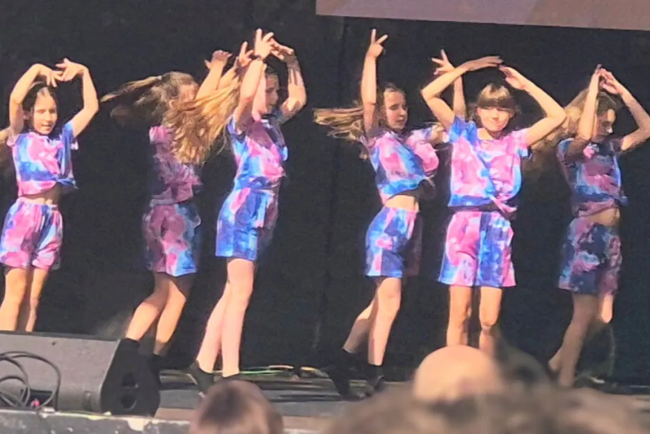 Mädchen in lila Outfits tanzen auf einer Bühne. 