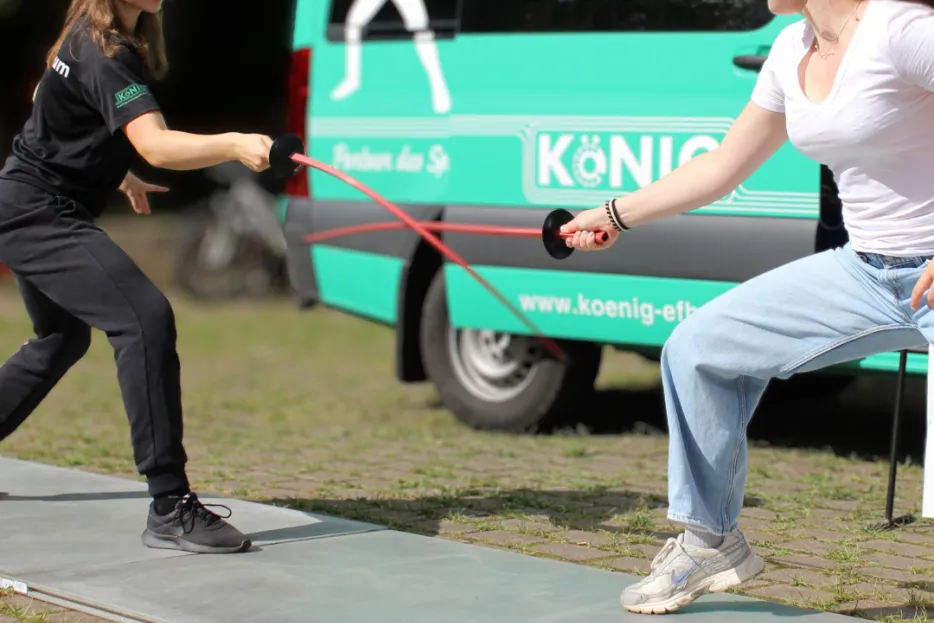 Zwei junge Damen fechten vor einem grünen Transporter.