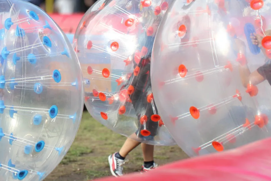 Bubble Ball: Drei Menschen in aufgeblasenen Gummibällen laufen einem Ball nach.