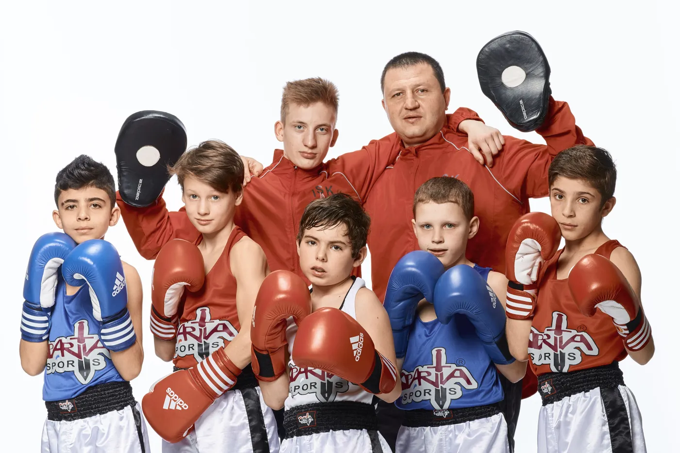 Ein Boxtrainer posiert mit sechs jungen Sportlern unterschiedlichen Alters und unterschiedlicher Hautfarbe. Alle tragen Boxhandschuhe.