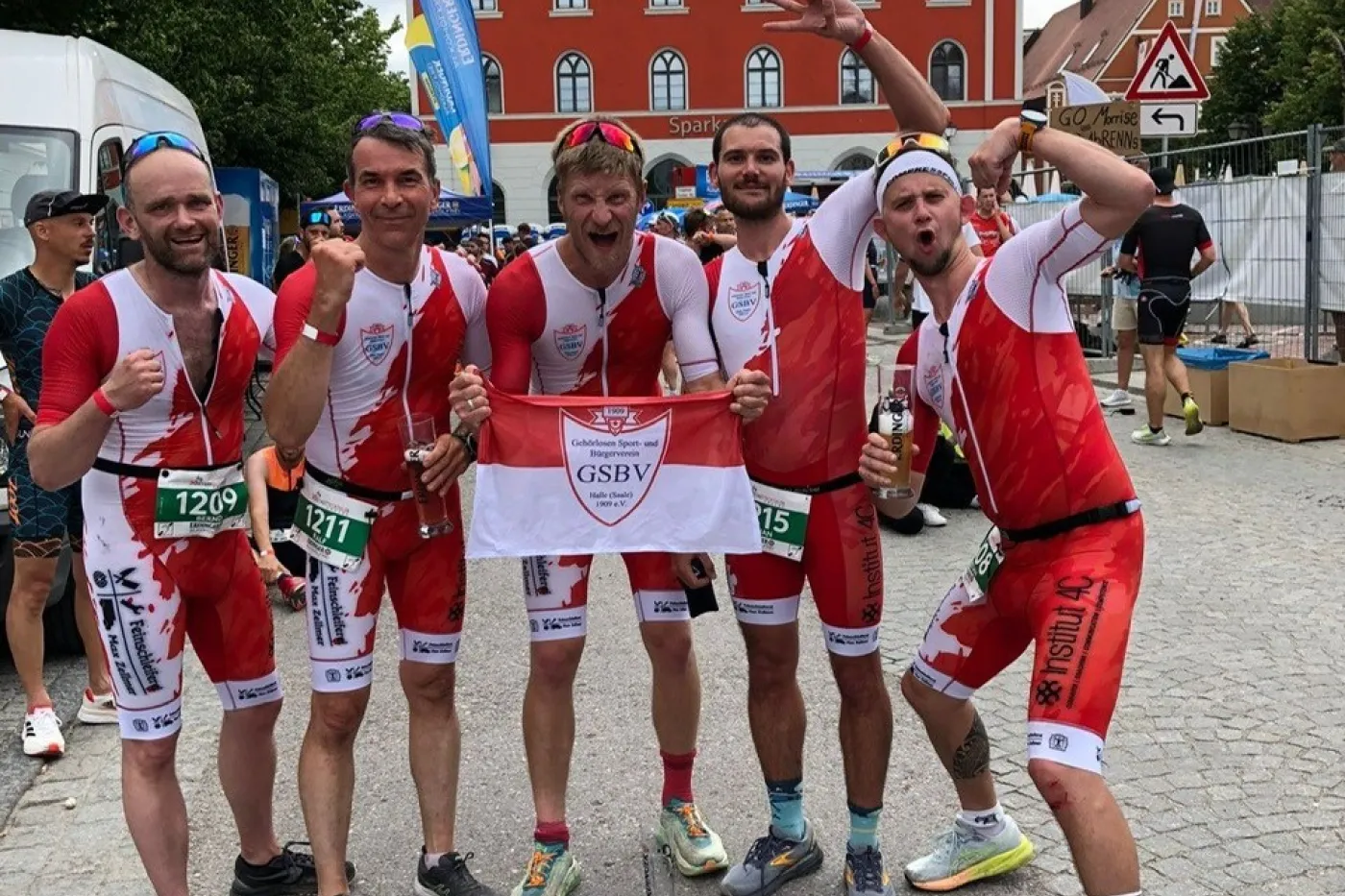 GSBV Halle Triathleten Bernd Kaiser, Ralf Bernhardt, Max Zellmer, Yohan Marcelino und Sebastian Schölzel jubeln in rot-weißen Sportanzügen in die Kamera.