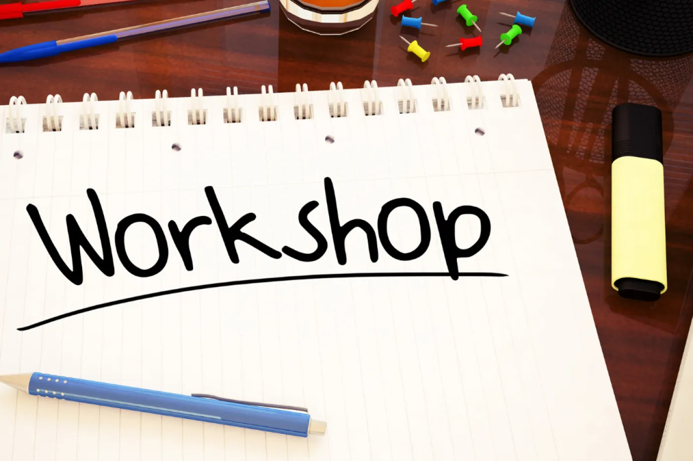 Workshop Symbolbild Schreibblock mit Aufschrift "Workshop", Stifte und Pinnnadeln auf einem Tisch.