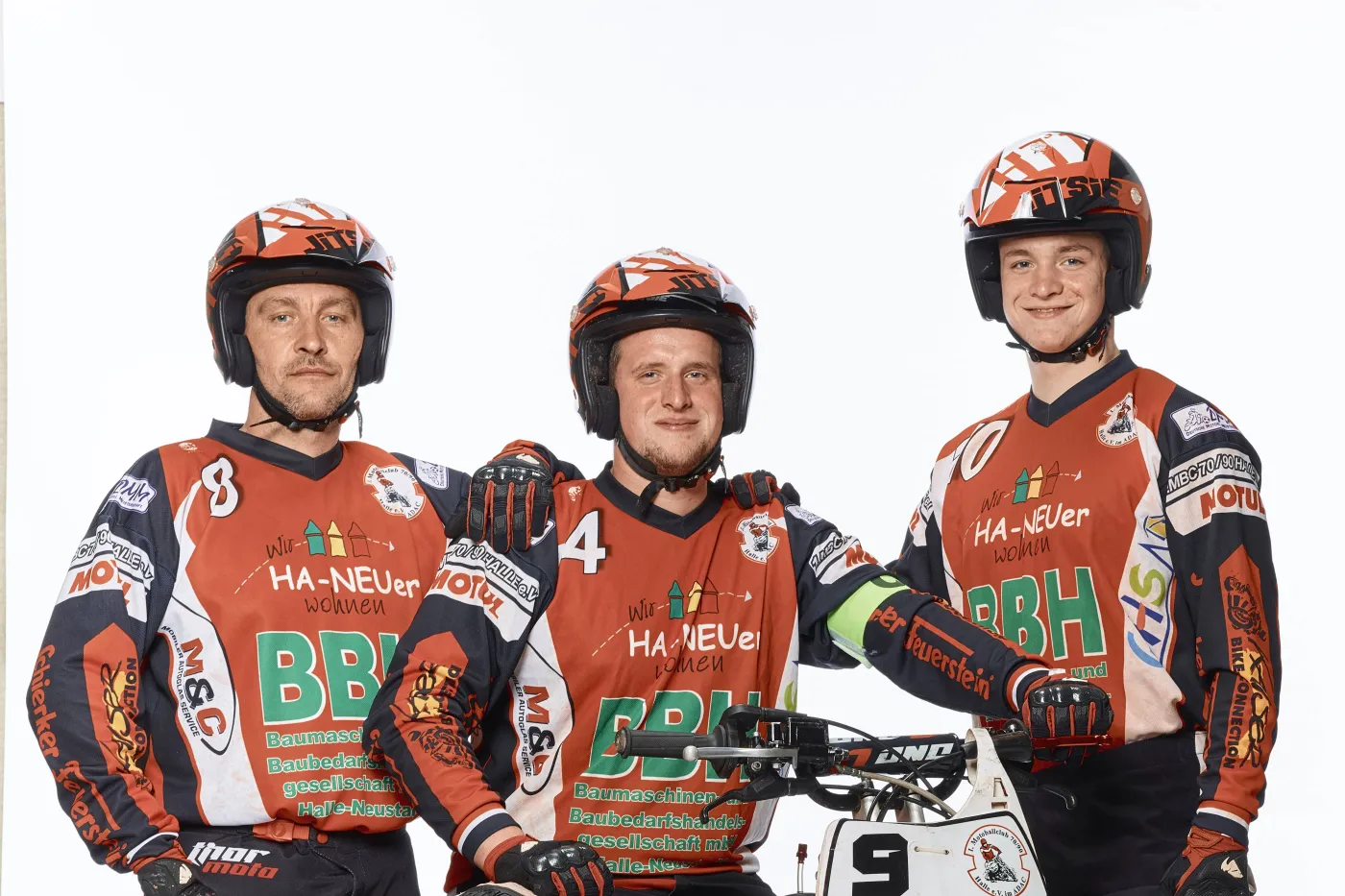 Motoball Drei Motoballer posieren in Wettkampfkleidung mit einem Motorrad und Ball.