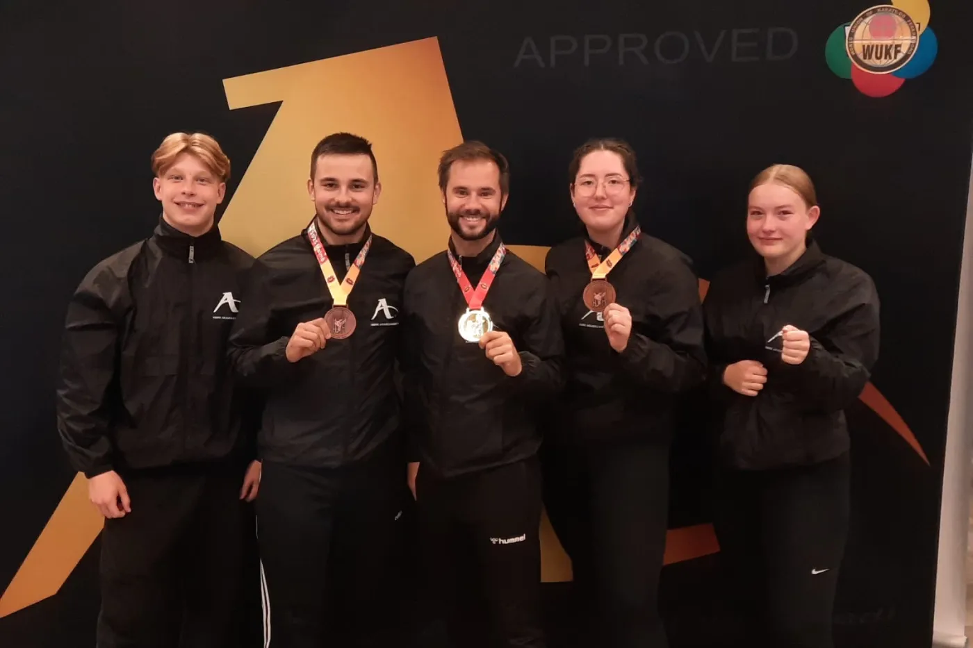 KIH Medaillen die 5 Teilnehmer des KIH posieren in dunkler Kleidung für die Kamera, 3 von ihnen mit Medaille.