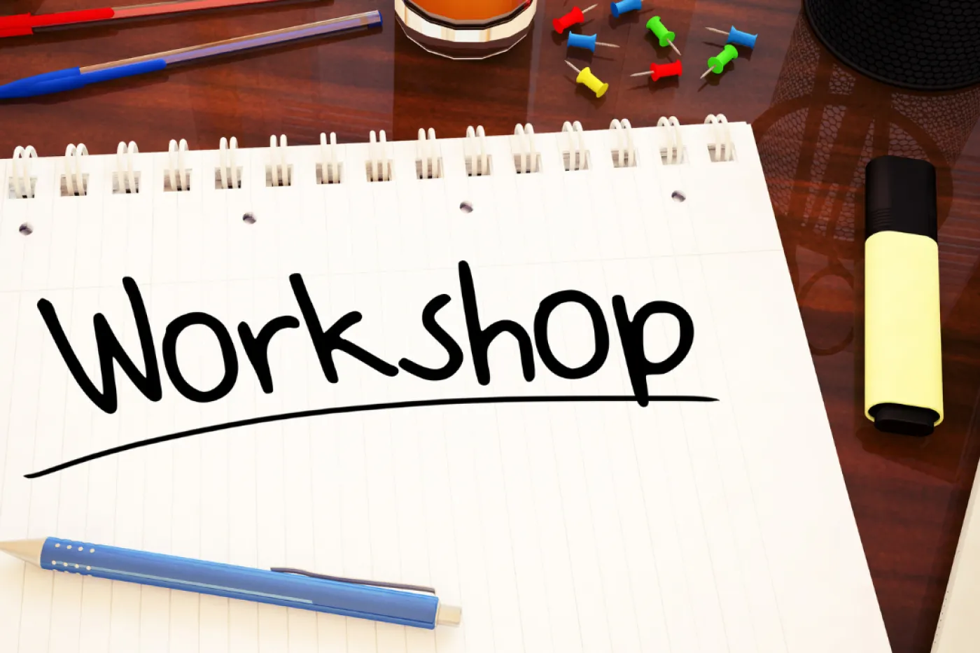 Auf einem Tisch liegt ein Block mit dem Schriftzug "Workshop", daneben Stifte und ein Glas Saft.