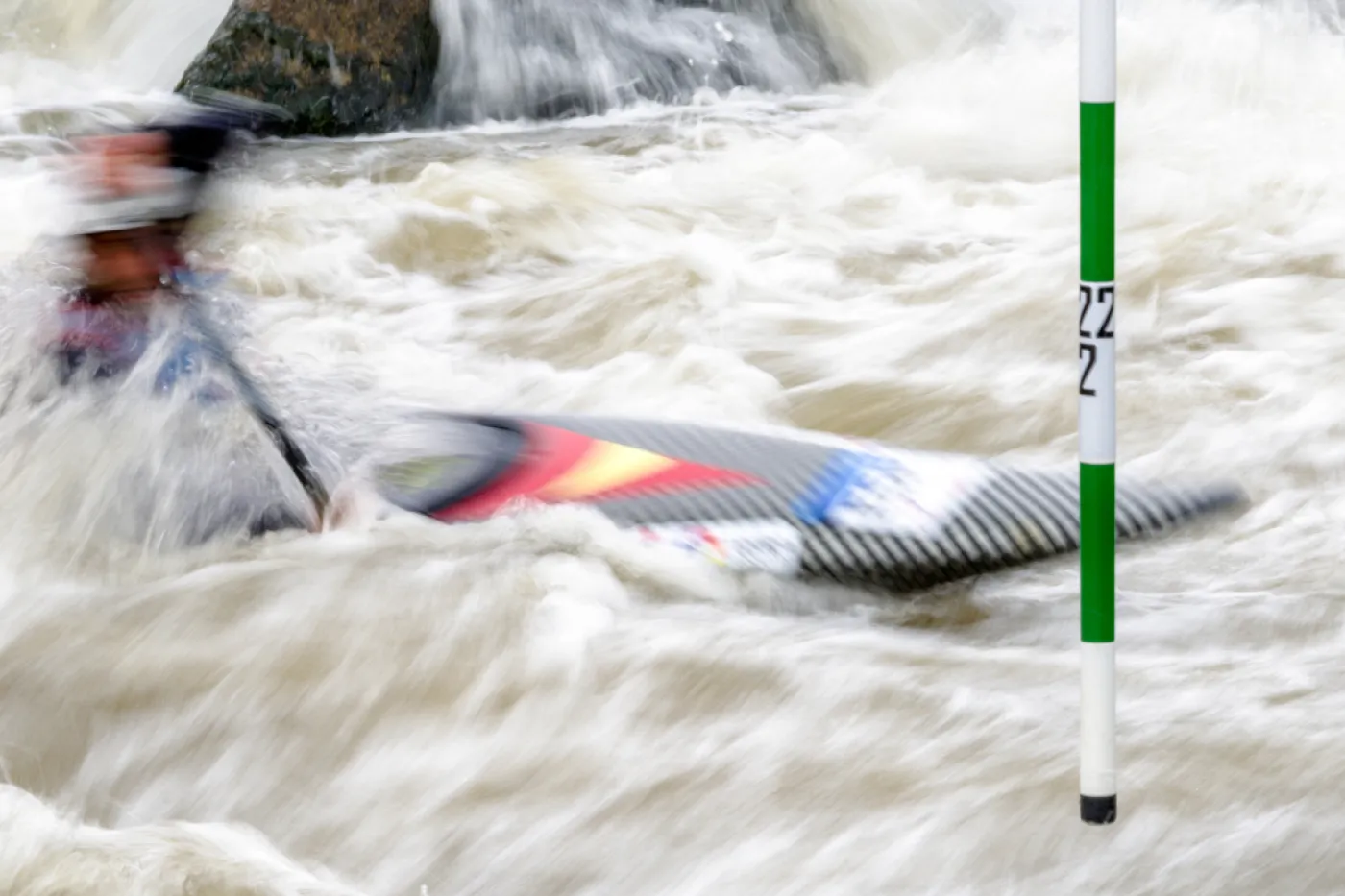 Symboldbild Kanuslalom Ein Kajak beim Kanuslalom vor einer grün-weißen Stange.