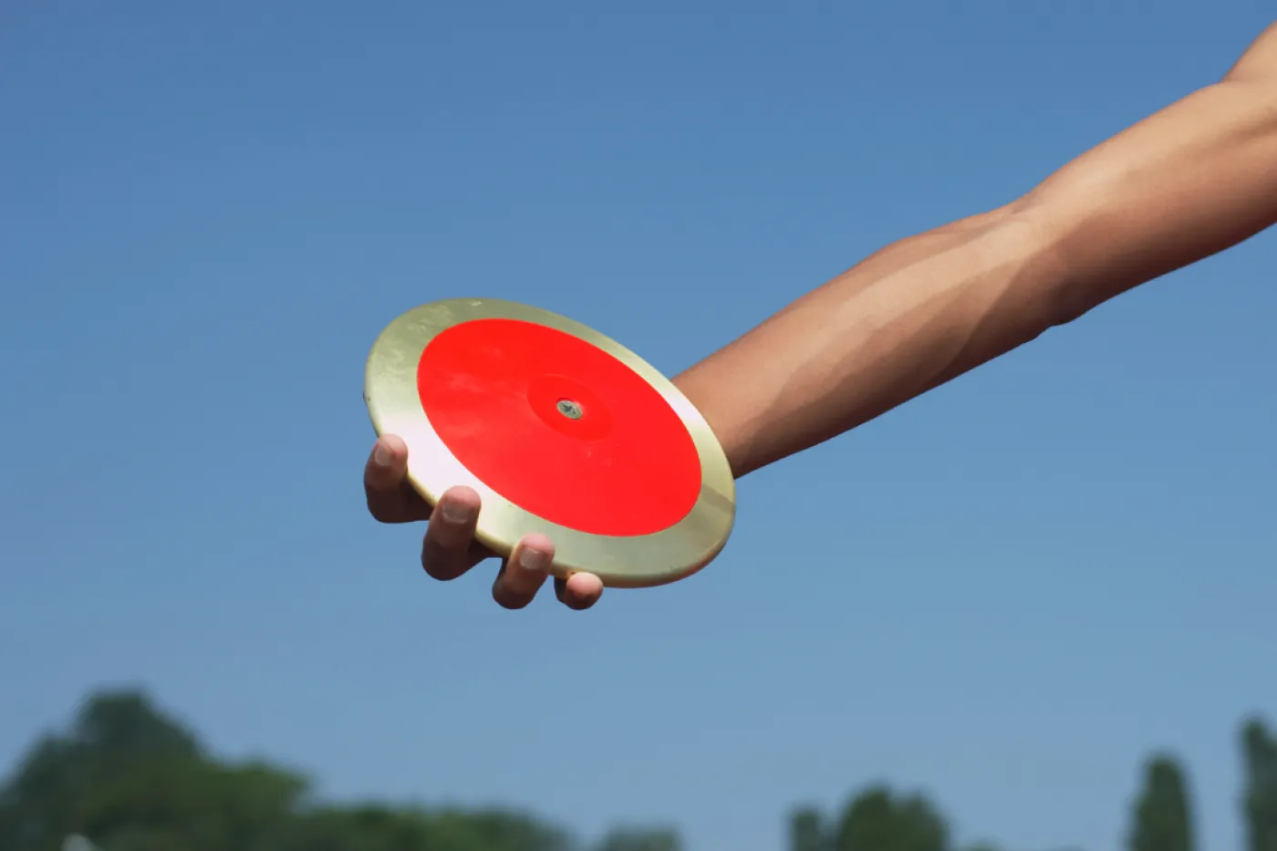 Diskus Ein arm mit einer roten Diskusscheibe vor blauem Himmel.