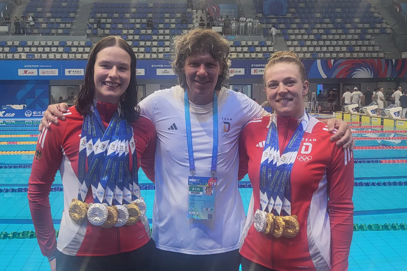 Oppermann und Lauerwald mit ihren Medaillen neben Team-Manager Holger Friedrich in der Schwimmhalle.