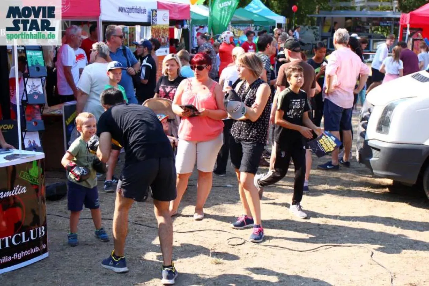 Sportwiese Sportwiese: Menschen flanieren an Zelten vorbei, im Vordergrund probiert sich ein Kind im Boxen.