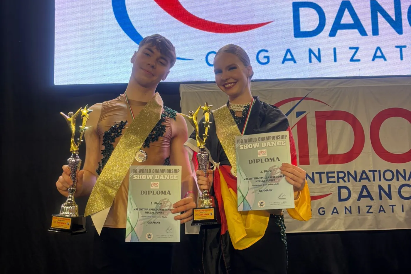 Funke und Wiesener mit Pokal, Urkunde und Deutschlandfahne bei der Siegerehrung.