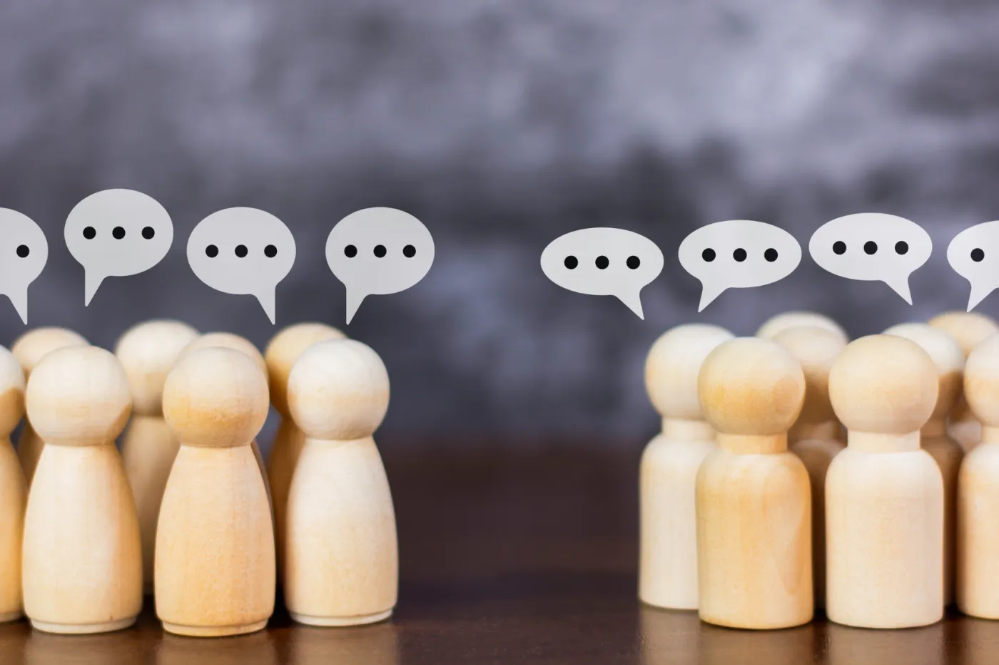 kleine Holzfiguren stehen sich in zwei Gruppen gege&uuml;ber und haben Sprechblasen &uuml;ber ihren K&ouml;pfen