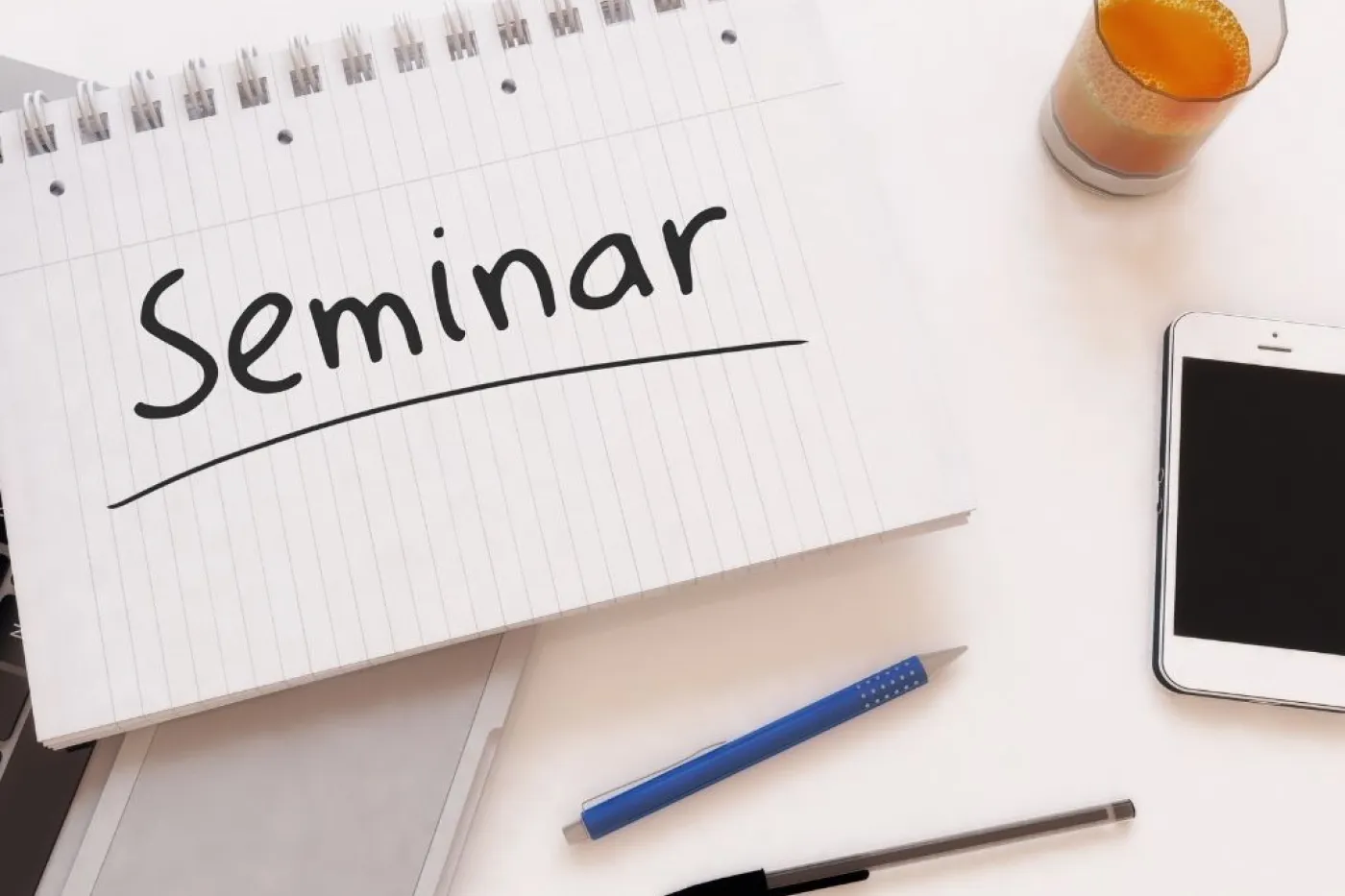 Stifte, Glas, Handy und Block mit Ausschrift Seminar auf Schreibtisch