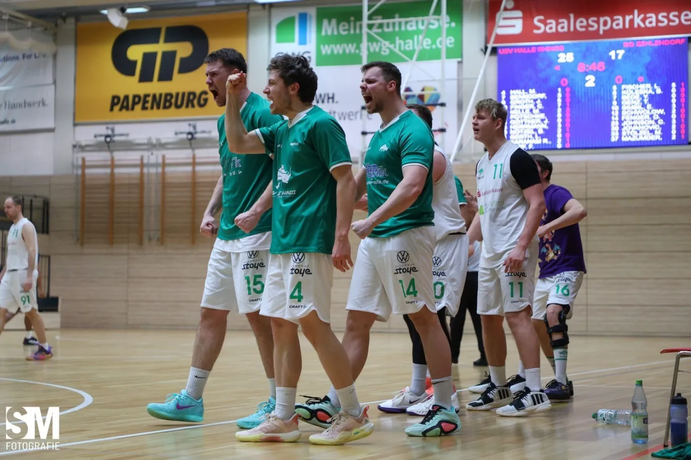 Drei Basketballer in gr&uuml;nen Trikots jubeln an der Seitenlinie