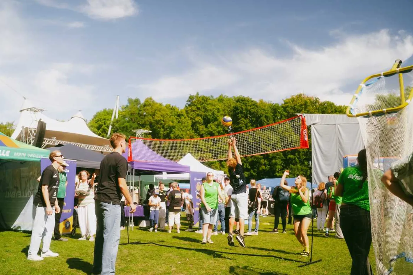 Menschen spielen Volleyball auf Wiese mit vielen St&auml;nden